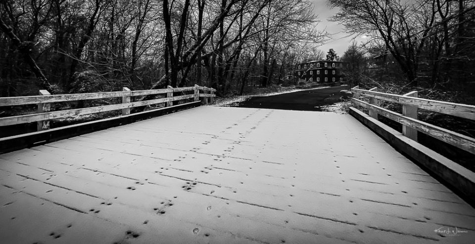 Wooden bridge in the snow with Kingston Mill in the background