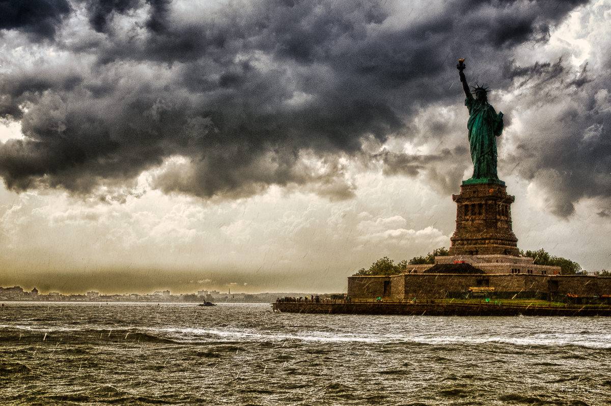 Statue Of Liberty in the rain. The sky is full of clouds. The clouds are moody and drak.